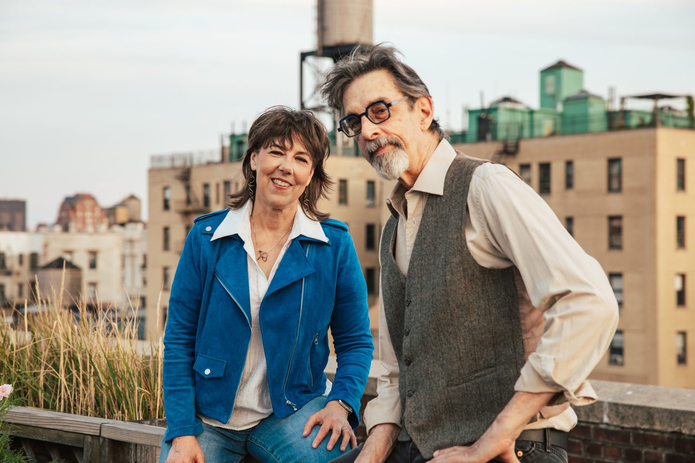 Beth Falcone, in a blue jacket, and Ritt Henn on a rooftop with water towers behind them.