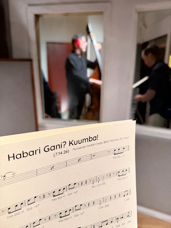 The Habari Gani? Kuumba! score in the foreground, with Ritt Henn on upright bass through the studio window.