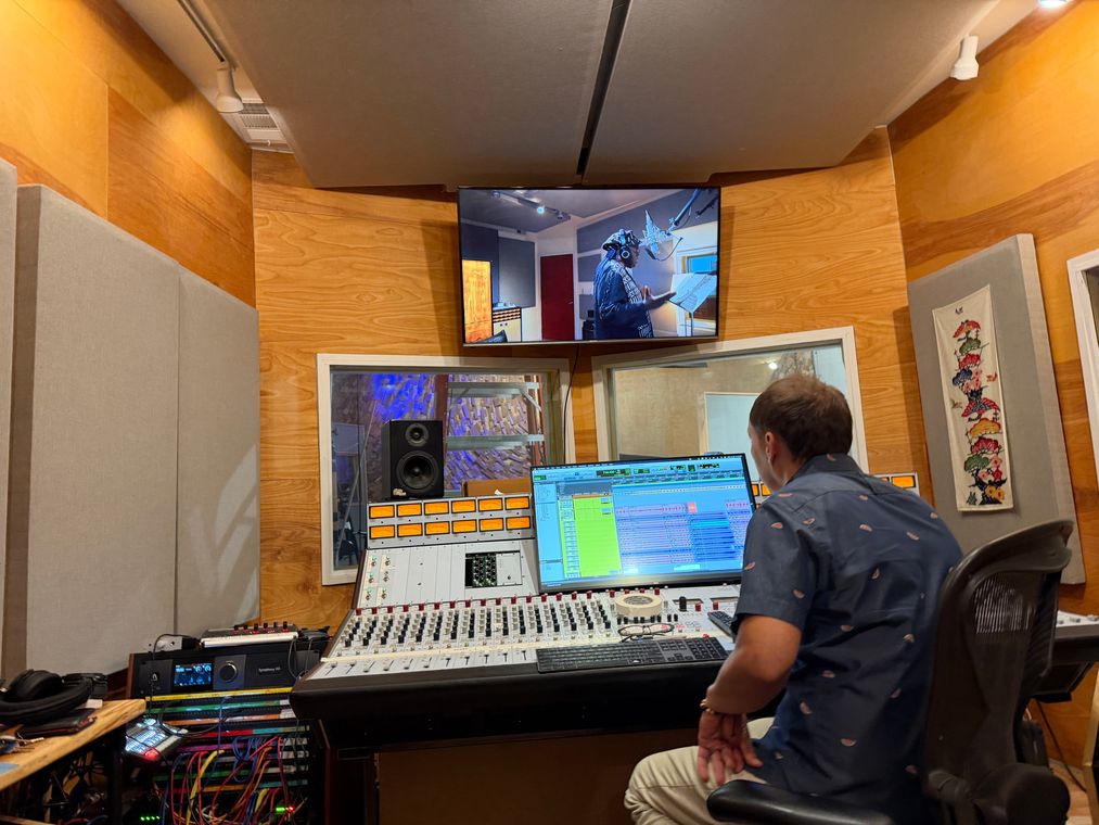 An engineer at the mixing console, watching the vocal booth on the monitor.