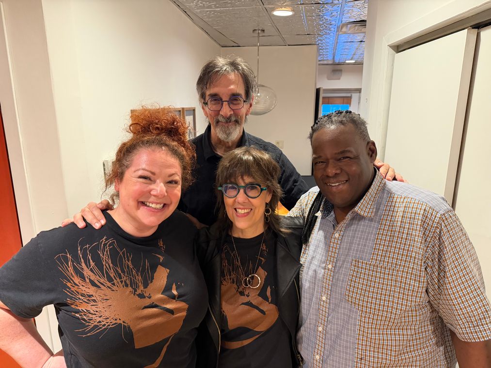 Four people smiling together in the studio hallway.