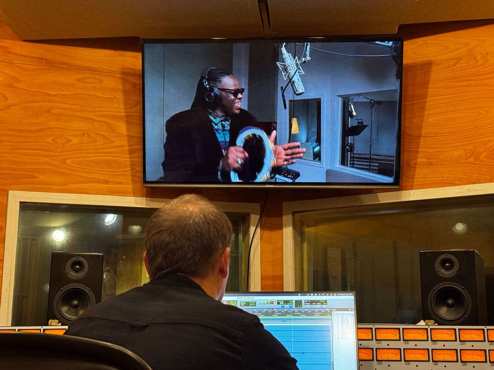 An engineer at the console while the monitor shows Roosevelt Andr&eacute; Credit singing with a tambourine.