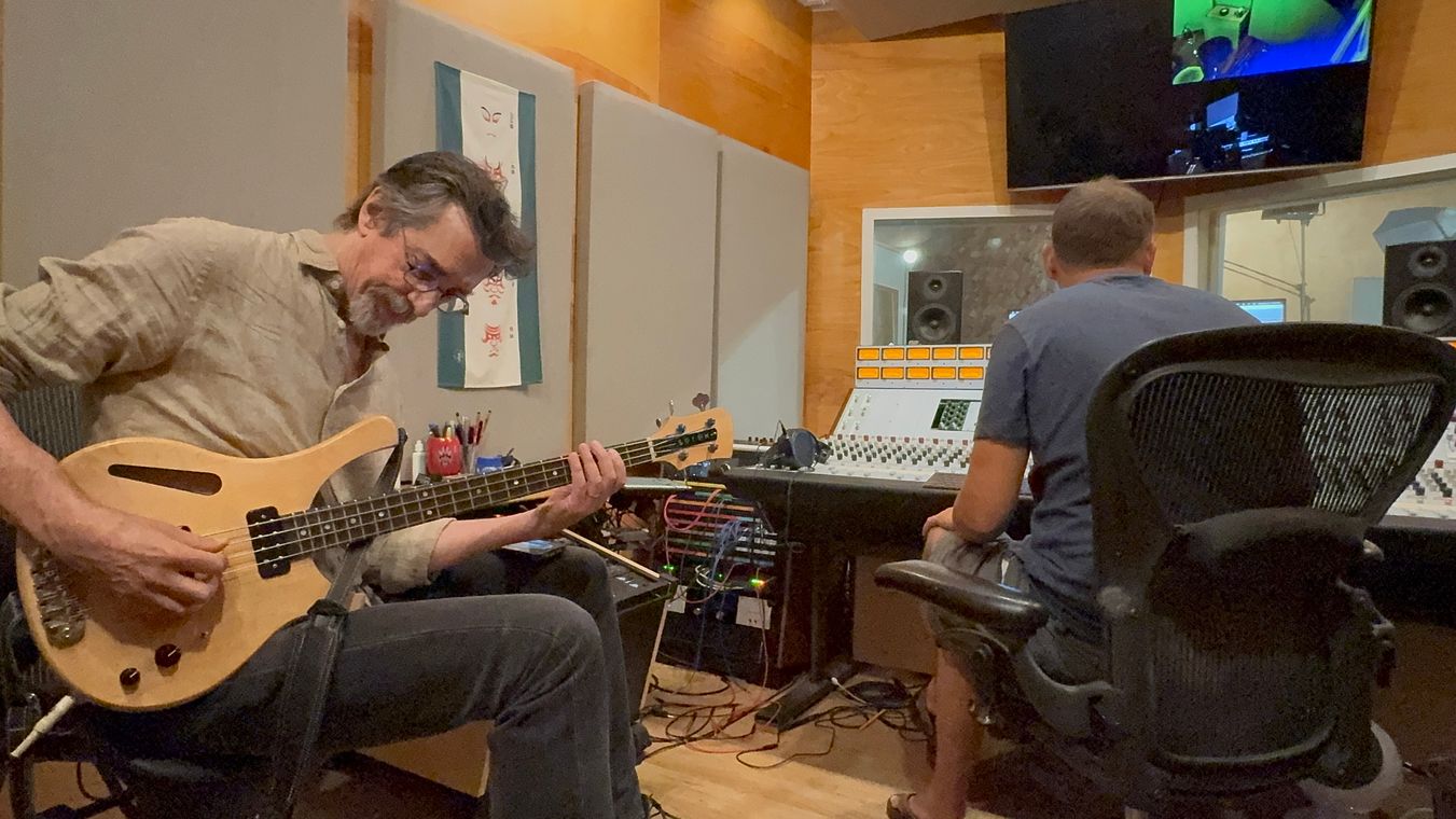 Ritt Henn playing electric bass in the control room while the engineer works at the console.