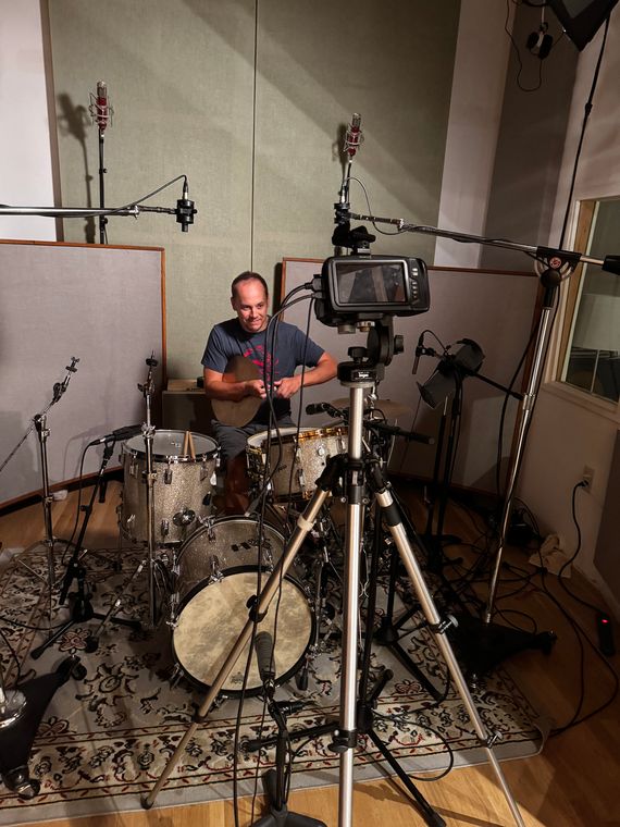 David Stoller at the drum kit in the live room, with a video camera set up in front.