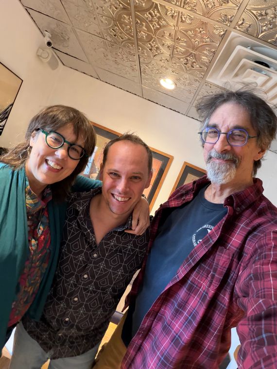 Three people smiling in a selfie in the studio hallway.