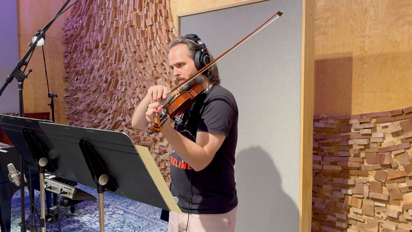 Reid Jenkins playing violin in the live room, in front of the studio&rsquo;s wooden wave wall.